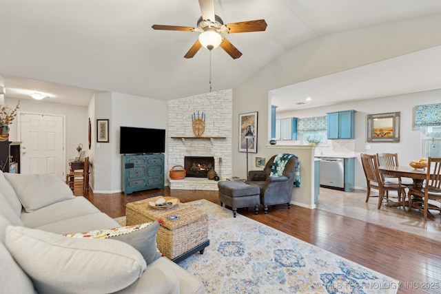 living room with ceiling fan, lofted ceiling, dark hardwood / wood-style flooring, and a stone fireplace