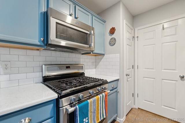 kitchen featuring blue cabinets, appliances with stainless steel finishes, light tile patterned floors, and decorative backsplash