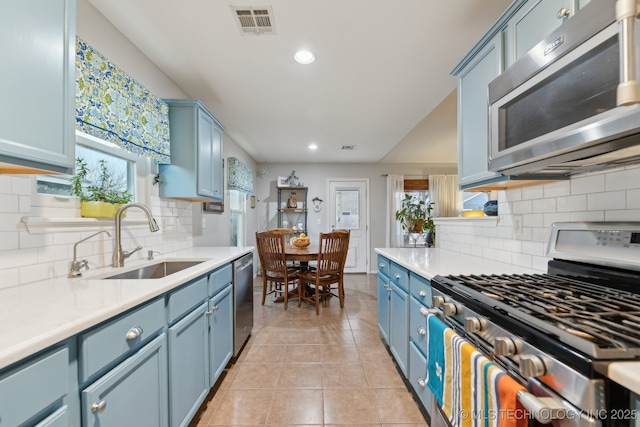 kitchen with appliances with stainless steel finishes, sink, light tile patterned floors, and blue cabinetry