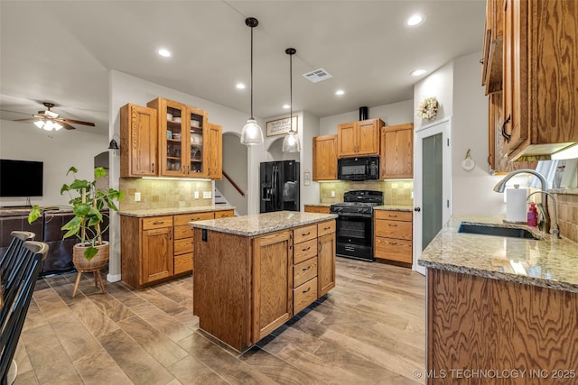 kitchen with sink, hanging light fixtures, a center island, black appliances, and light stone countertops