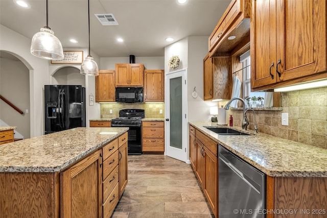 kitchen with sink, black appliances, light stone countertops, a kitchen island, and decorative light fixtures