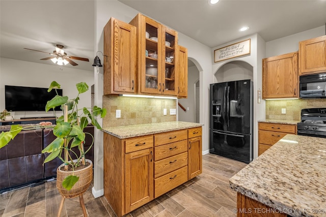 kitchen featuring tasteful backsplash, light stone countertops, black appliances, and ceiling fan