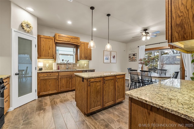 kitchen featuring sink, decorative backsplash, hanging light fixtures, a center island, and light stone countertops