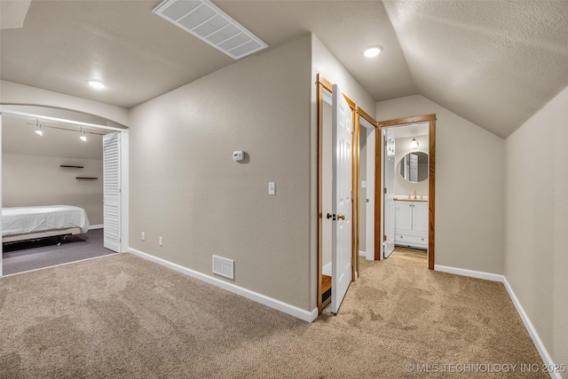 unfurnished bedroom with lofted ceiling, sink, light carpet, and a textured ceiling