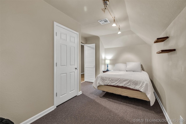 bedroom with vaulted ceiling, track lighting, and dark carpet