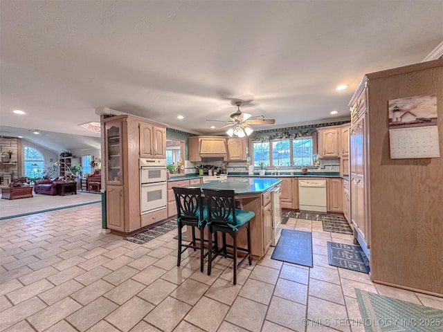 kitchen featuring light brown cabinetry, open floor plan, a kitchen island, white appliances, and a kitchen breakfast bar