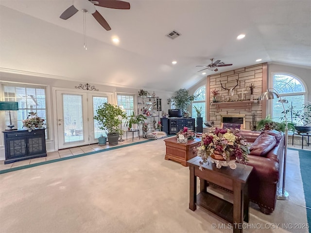 living area featuring lofted ceiling, a stone fireplace, a wealth of natural light, and visible vents