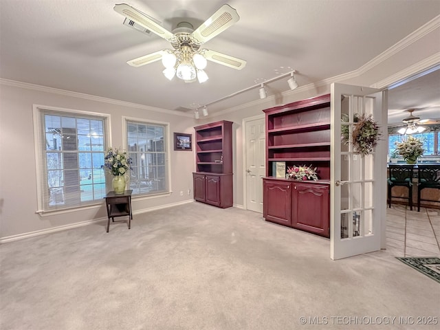 interior space with ceiling fan, light carpet, crown molding, baseboards, and track lighting