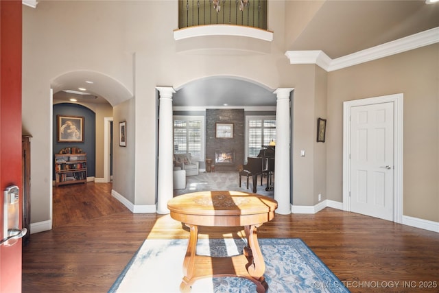 entrance foyer featuring ornate columns, a large fireplace, ornamental molding, dark hardwood / wood-style flooring, and a high ceiling