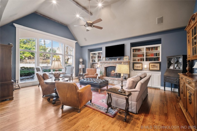 living room with hardwood / wood-style flooring, a stone fireplace, ceiling fan, built in shelves, and vaulted ceiling