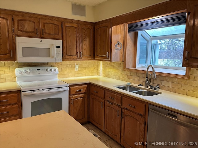 kitchen with sink, white appliances, light tile patterned floors, and backsplash