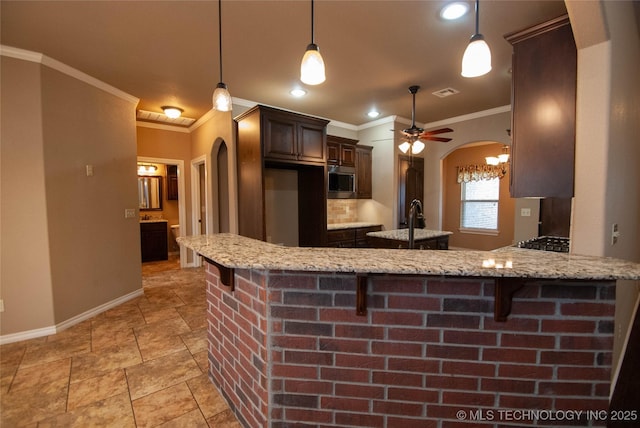 kitchen featuring dark brown cabinetry, a kitchen bar, decorative light fixtures, stainless steel microwave, and kitchen peninsula