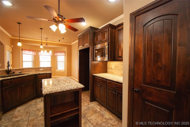 kitchen with sink, crown molding, stainless steel microwave, light stone counters, and dark brown cabinetry