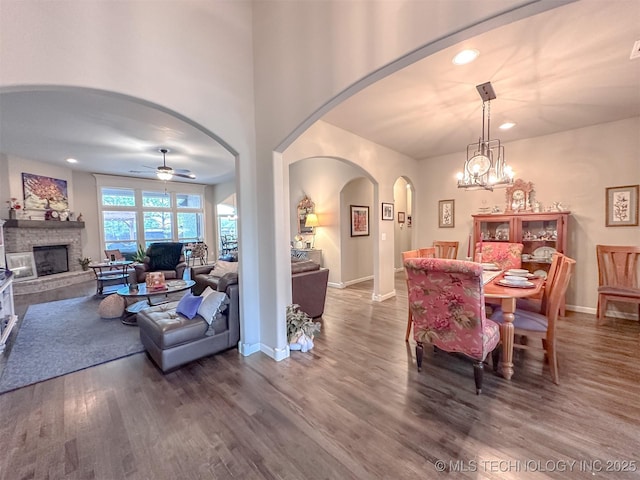 dining area with dark hardwood / wood-style floors, ceiling fan with notable chandelier, and a stone fireplace