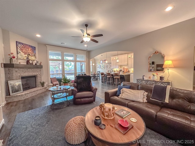 living room featuring ceiling fan, a brick fireplace, and dark hardwood / wood-style flooring