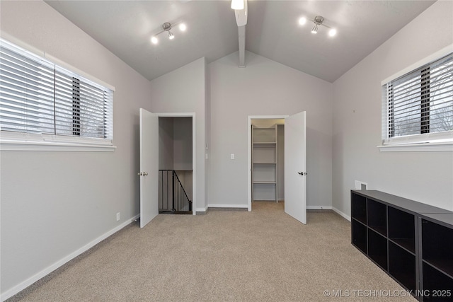 unfurnished bedroom featuring multiple windows, a spacious closet, light carpet, and vaulted ceiling with beams