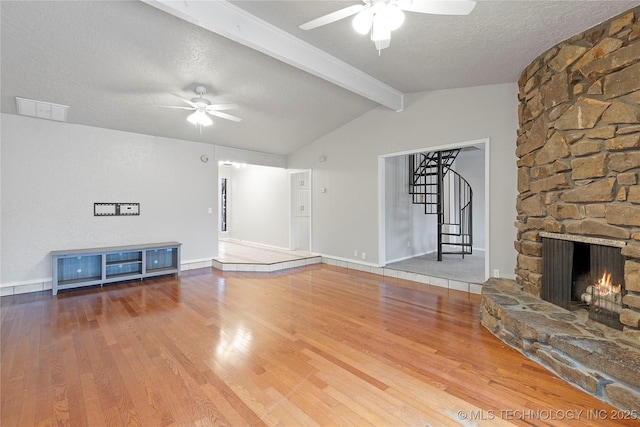 unfurnished living room with ceiling fan, hardwood / wood-style floors, vaulted ceiling with beams, a textured ceiling, and a stone fireplace