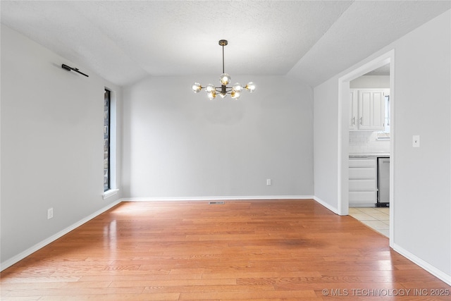 unfurnished room featuring an inviting chandelier, vaulted ceiling, a textured ceiling, and light wood-type flooring