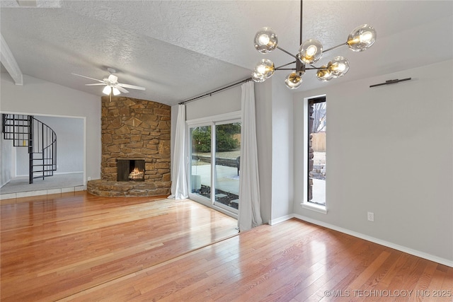 unfurnished living room with ceiling fan with notable chandelier, a fireplace, wood-type flooring, lofted ceiling, and a textured ceiling