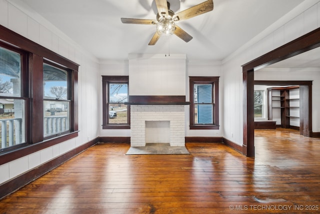 unfurnished living room featuring a brick fireplace, crown molding, dark hardwood / wood-style floors, and ceiling fan