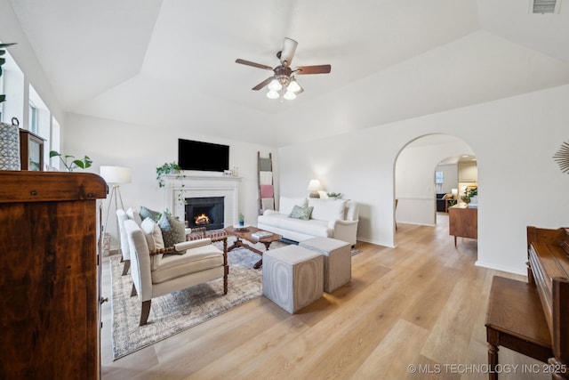 living room featuring ceiling fan, a brick fireplace, vaulted ceiling, a raised ceiling, and light wood-type flooring