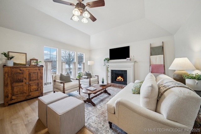 living room with ceiling fan, a brick fireplace, vaulted ceiling, and light hardwood / wood-style flooring