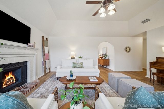 living room featuring ceiling fan, lofted ceiling, a fireplace, and light hardwood / wood-style floors