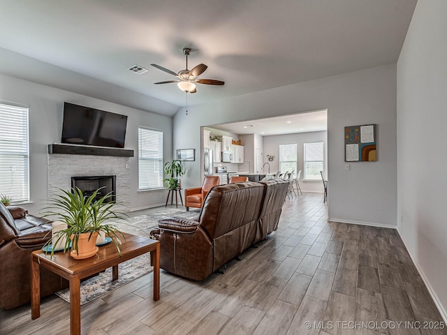 living room featuring a fireplace, plenty of natural light, ceiling fan, and light wood-type flooring