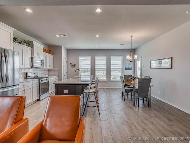 kitchen with a breakfast bar, pendant lighting, white cabinetry, a kitchen island with sink, and stainless steel appliances