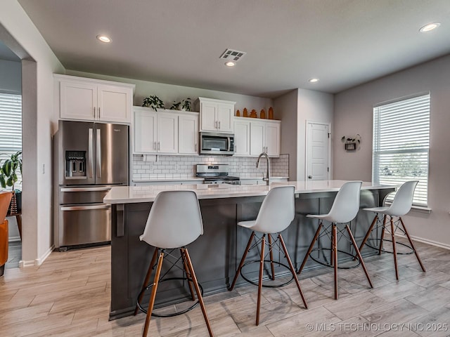 kitchen with appliances with stainless steel finishes, white cabinetry, a kitchen breakfast bar, an island with sink, and decorative backsplash