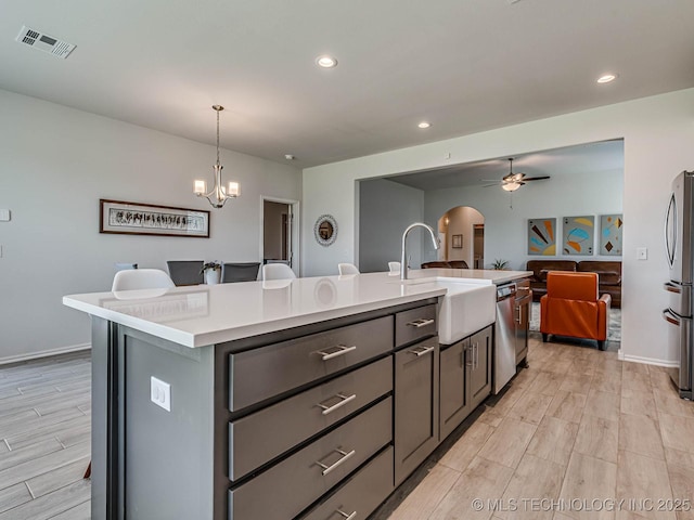 kitchen featuring sink, decorative light fixtures, appliances with stainless steel finishes, an island with sink, and ceiling fan with notable chandelier