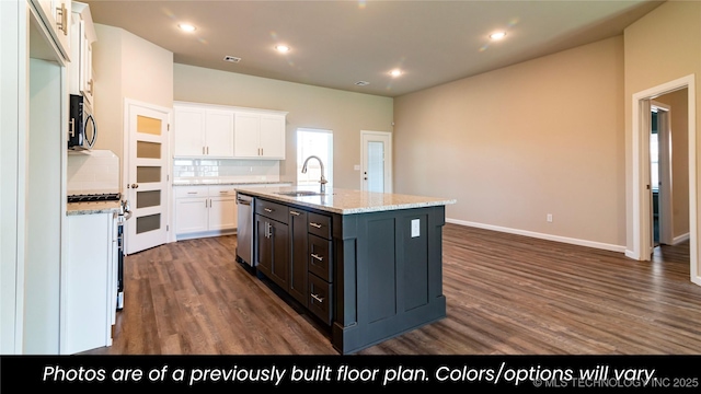 kitchen with sink, appliances with stainless steel finishes, white cabinetry, light stone counters, and a center island with sink