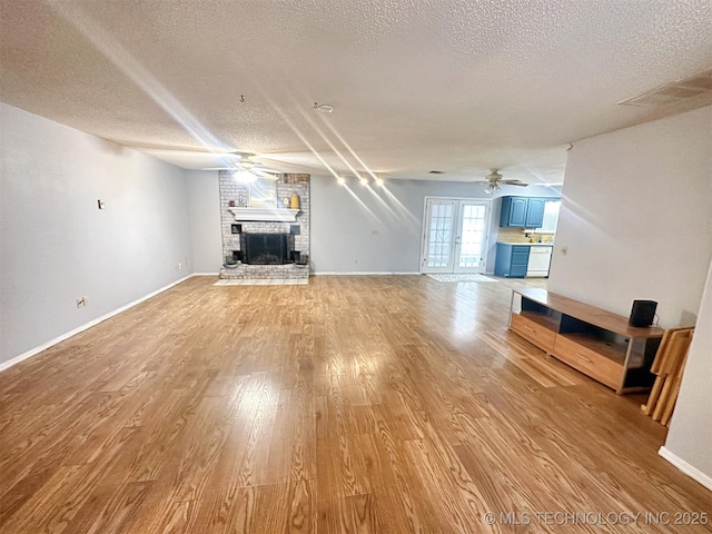 unfurnished living room with light wood-type flooring, ceiling fan, a brick fireplace, a textured ceiling, and french doors