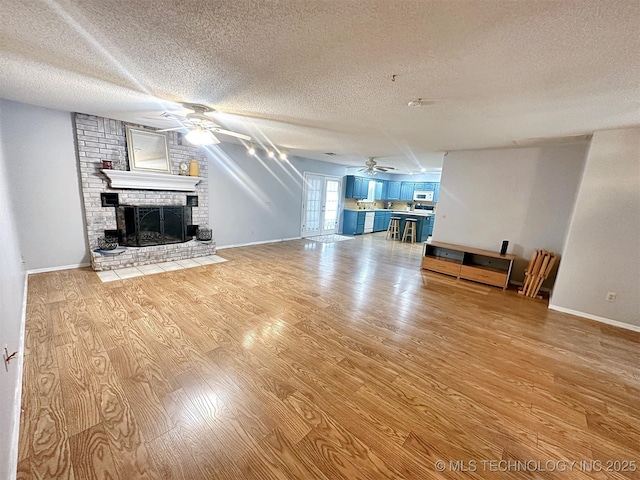 unfurnished living room with a textured ceiling, a fireplace, ceiling fan, and light wood-type flooring