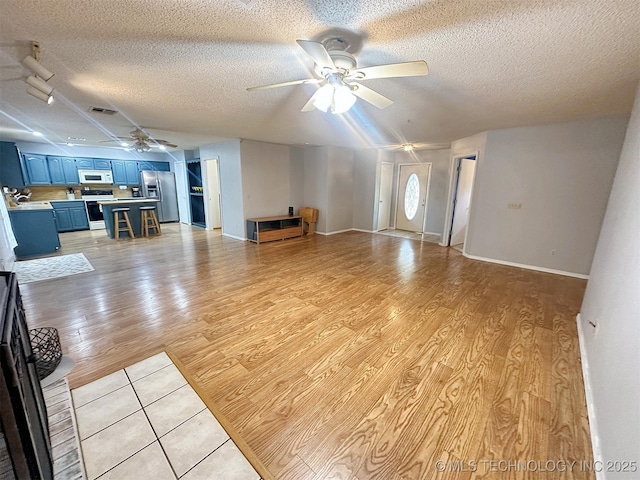 unfurnished living room with ceiling fan, light hardwood / wood-style flooring, and a textured ceiling