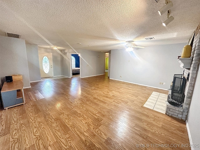 unfurnished living room with ceiling fan, light hardwood / wood-style floors, a brick fireplace, and a textured ceiling