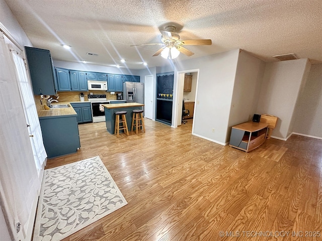 kitchen featuring range with electric stovetop, stainless steel fridge, a kitchen bar, blue cabinetry, and light wood-type flooring