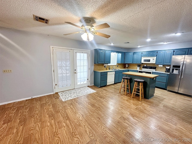 kitchen featuring blue cabinets, a breakfast bar area, a center island, light hardwood / wood-style floors, and white appliances