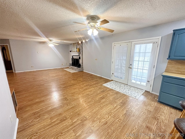 unfurnished living room featuring a fireplace, ceiling fan, light hardwood / wood-style floors, a textured ceiling, and french doors