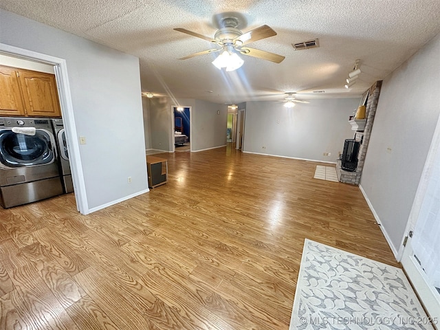 unfurnished living room featuring ceiling fan, independent washer and dryer, a fireplace, a textured ceiling, and light wood-type flooring