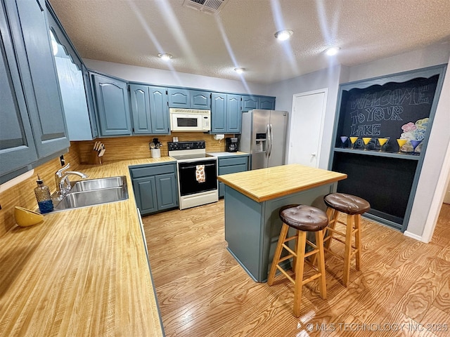 kitchen featuring a breakfast bar, blue cabinets, sink, white appliances, and light hardwood / wood-style flooring