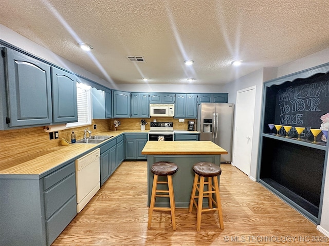 kitchen featuring white appliances, blue cabinetry, a kitchen breakfast bar, a center island, and light hardwood / wood-style floors