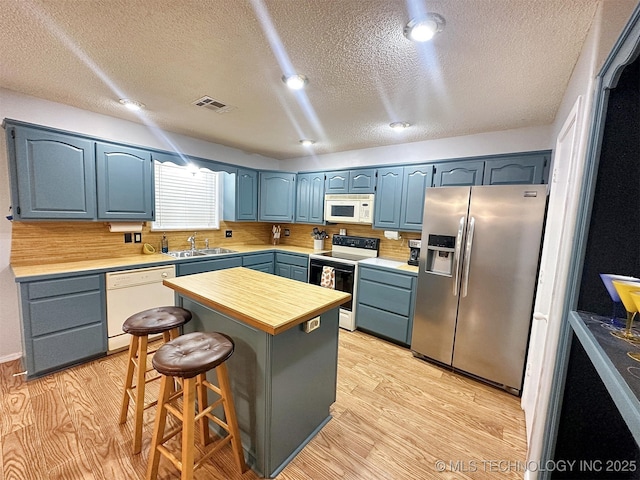 kitchen with blue cabinets, a breakfast bar area, light wood-type flooring, a kitchen island, and white appliances