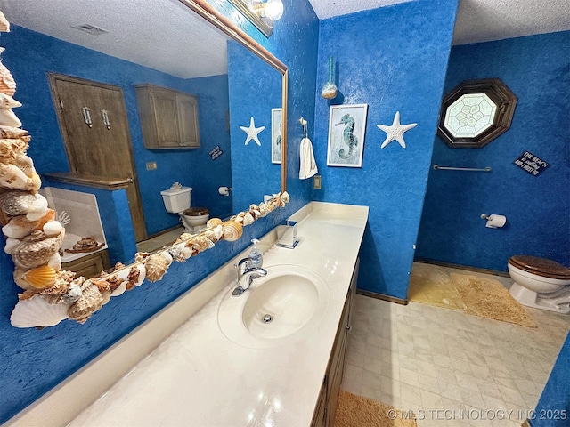 bathroom with vanity, toilet, and a textured ceiling