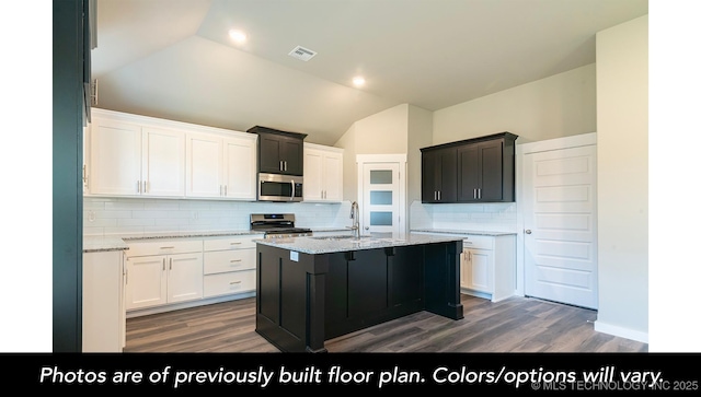 kitchen featuring white cabinetry, lofted ceiling, stainless steel appliances, and an island with sink