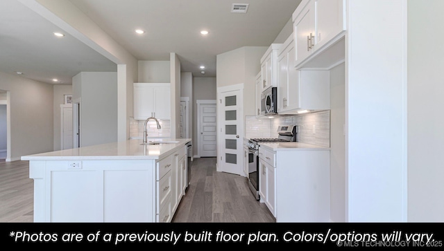 kitchen with appliances with stainless steel finishes, sink, white cabinets, a kitchen island with sink, and light wood-type flooring