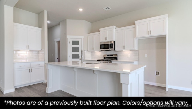 kitchen with white cabinetry, stainless steel appliances, sink, and a center island with sink