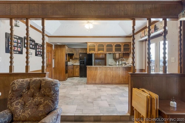 kitchen with wooden walls, black fridge with ice dispenser, sink, and kitchen peninsula