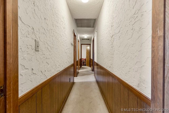 corridor featuring wooden walls, light colored carpet, and a textured ceiling