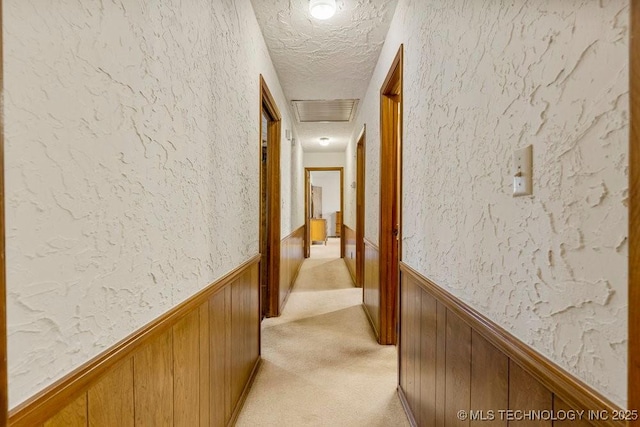 hallway with wooden walls, light carpet, and a textured ceiling